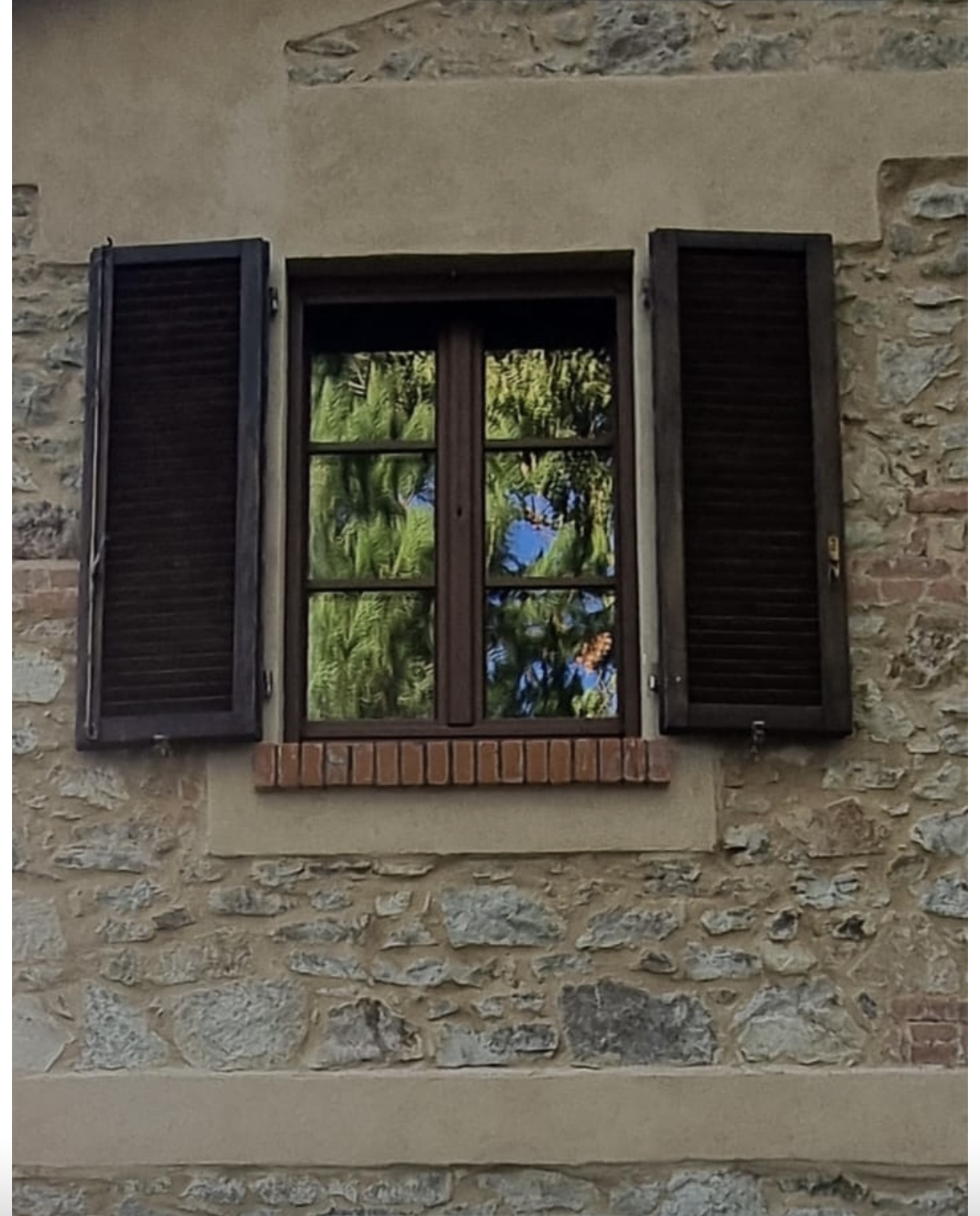 Finestra color legno con persiane su una facciata in pietra, installazione Giumar